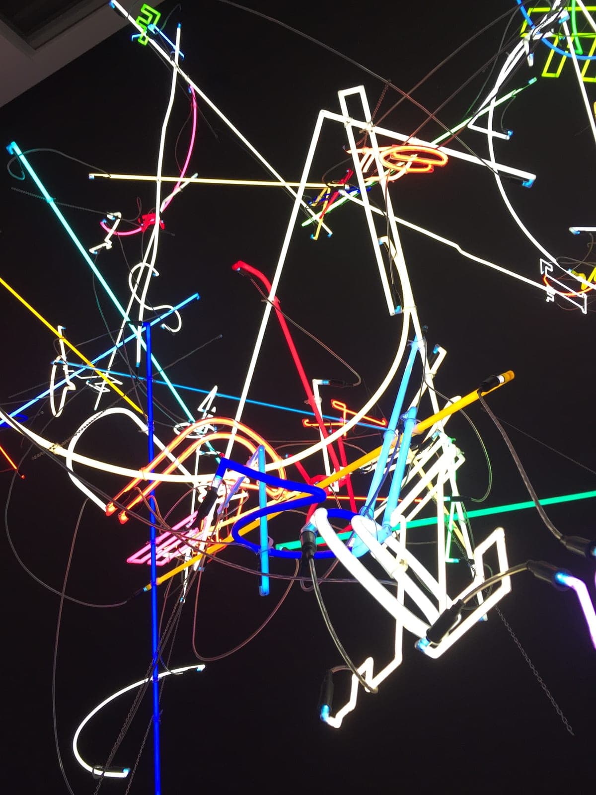 A tangle of glowing neon light tubes in white, red, blue, yellow and green against a black background.